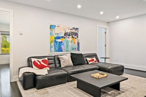 Una sala de estar moderna con un sofá seccional de cuero negro, una mesa de centro y un cuadro abstracto grande en la pared.