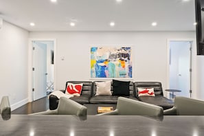 Une salle de réunion moderne, dotée d’un canapé en cuir noir, d’une table en verre et d’un grand tableau abstrait accroché au mur.