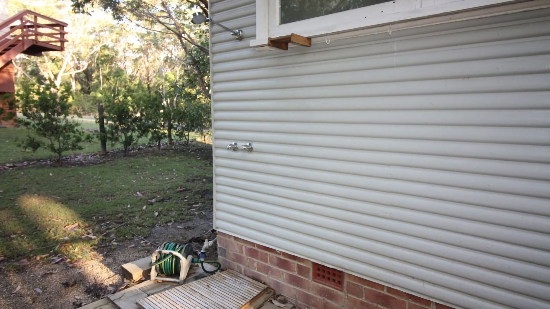 A house exterior with a garage door, a small wooden deck, and a hose reel.