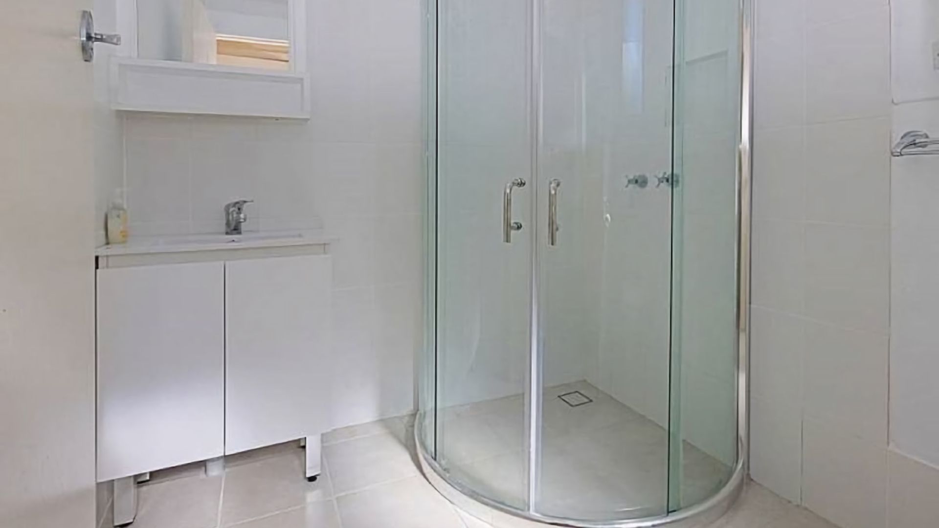 A bathroom with a glass shower enclosure, a white sink with a mirror above it, and a white cabinet below.
