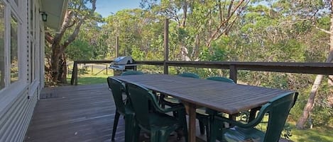 An outdoor deck with a wooden table and green chairs, surrounded by trees.