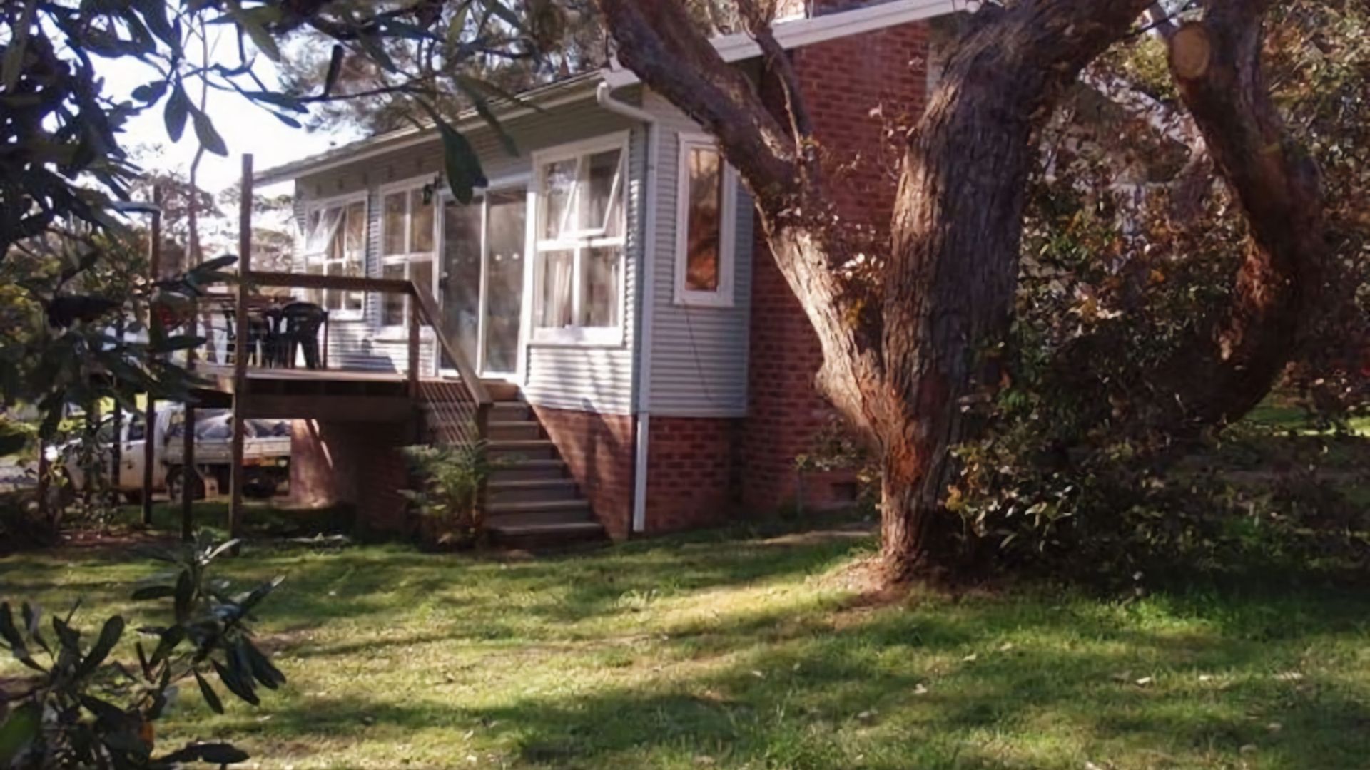 A two-story house with a front porch, a staircase leading to the second floor, and a large tree in the front yard.