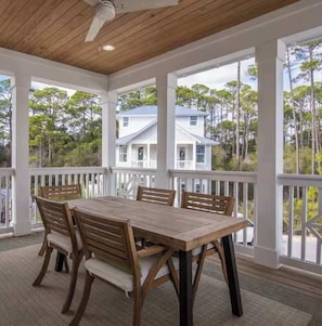 A covered outdoor dining area with a wooden table and chairs, white railings, and a view of a white house and trees. - Lotus by the Sea Seacrest 30A FL Pool, Beach Tram (Rosemary Beach)