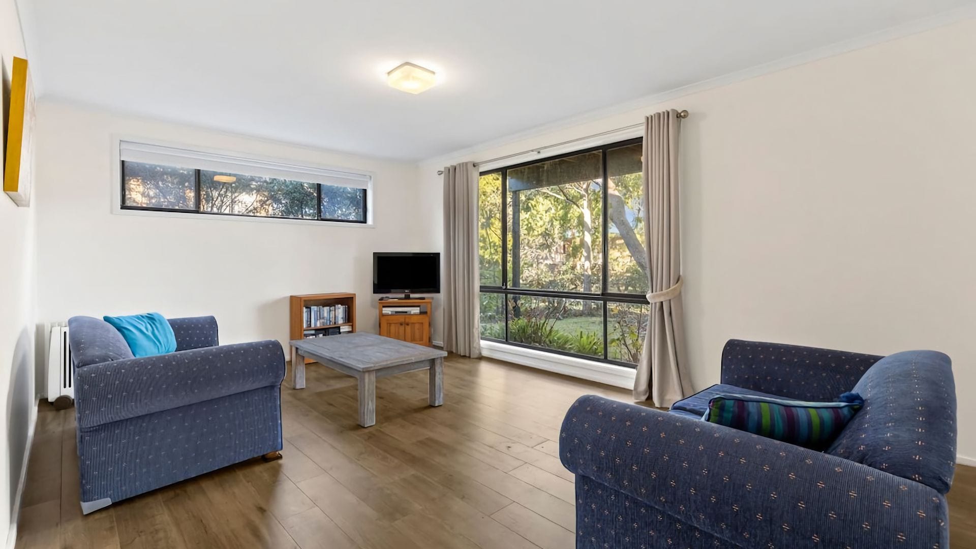 A living room with two sofas, a coffee table, a TV, and a large window with curtains.