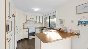 Una cocina compacta con armarios blancos, horno empotrado y encimera de madera.