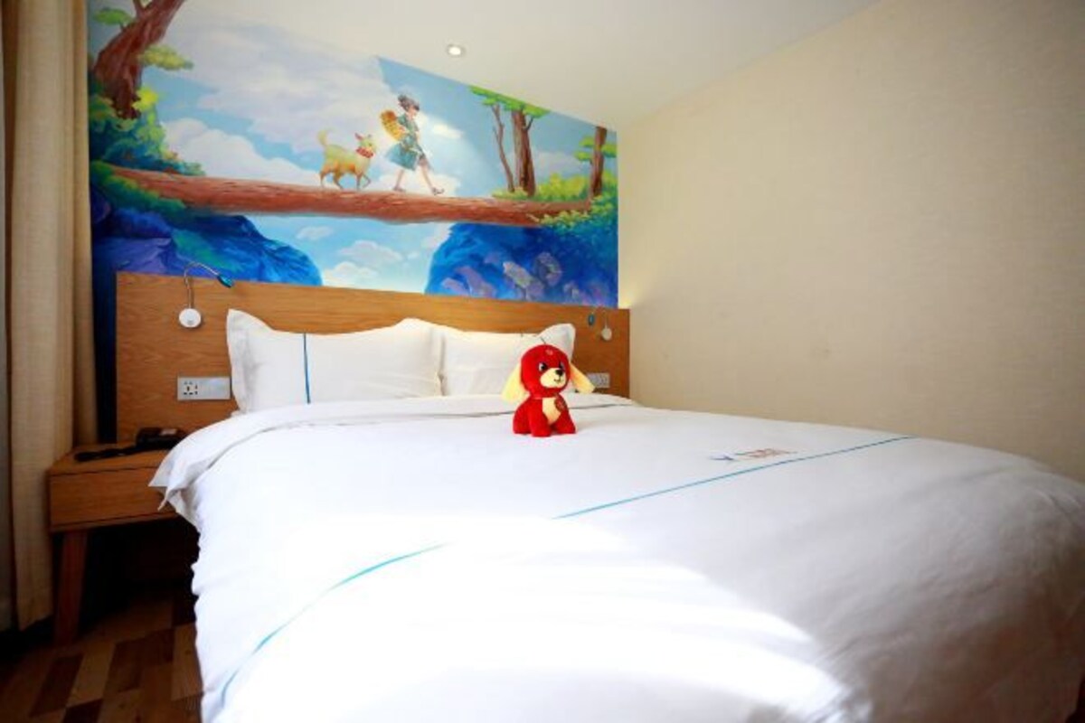 Habitación de hotel con una cama grande, una mesita de noche, un mural en la pared y un peluche rojo sobre la cama.