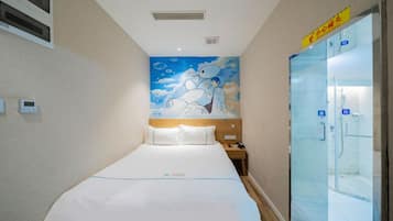 A hotel room with a bed, a nightstand, a wall mural, a bathroom with glass doors, and a sign above the door.
