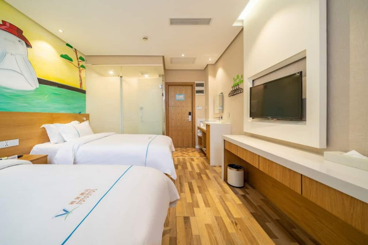 Ein Hotelzimmer mit zwei Betten, einem Fernseher, Holzboden und einem Gemälde an der Wand.