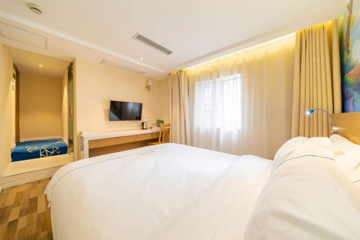 Ein Hotelzimmer mit einem großen Bett, einem Schreibtisch mit Fernseher und einem Fenster mit Vorhängen.