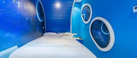 A room with a bed, a nightstand, and two circular windows with space-themed murals.
