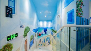 Un couloir d’hôtel orné d’une fresque aux motifs bleus, avec un escalier et un panneau indiquant le numéro de la chambre 202.