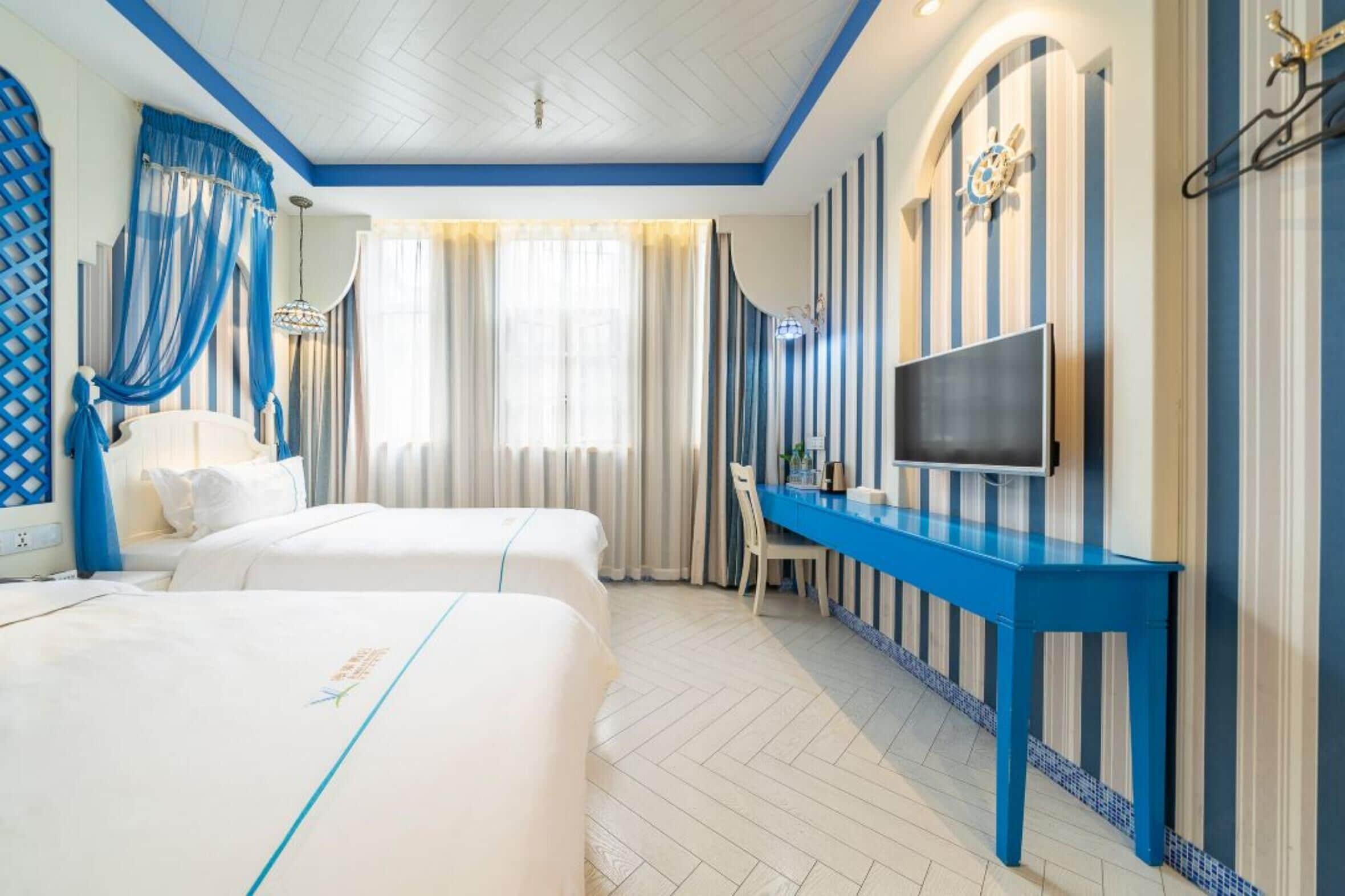 Ein Hotelzimmer mit zwei Betten, einem Schreibtisch, einem Fernseher und rautenförmig gemusterten Wänden.