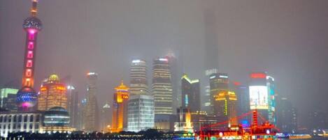 A nighttime cityscape with illuminated skyscrapers and a river with a brightly lit boat.