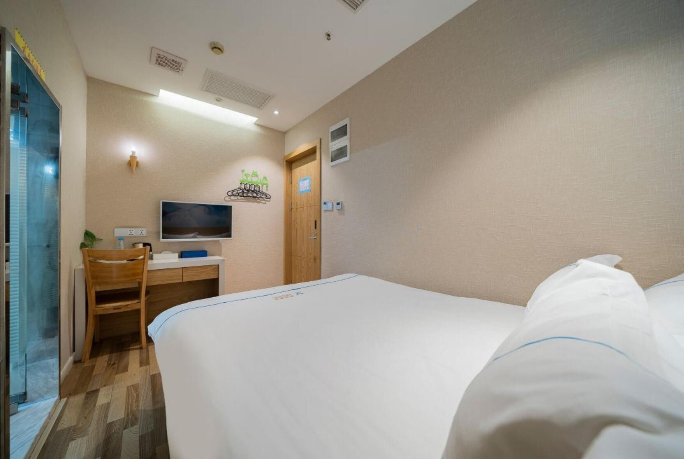 A hotel room with a bed, a desk with a computer, a chair, and a television.