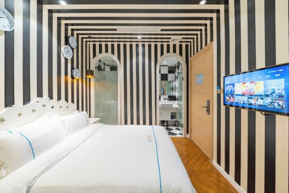 Habitación de hotel con una cama, un televisor y un baño visible a través de una puerta de cristal.