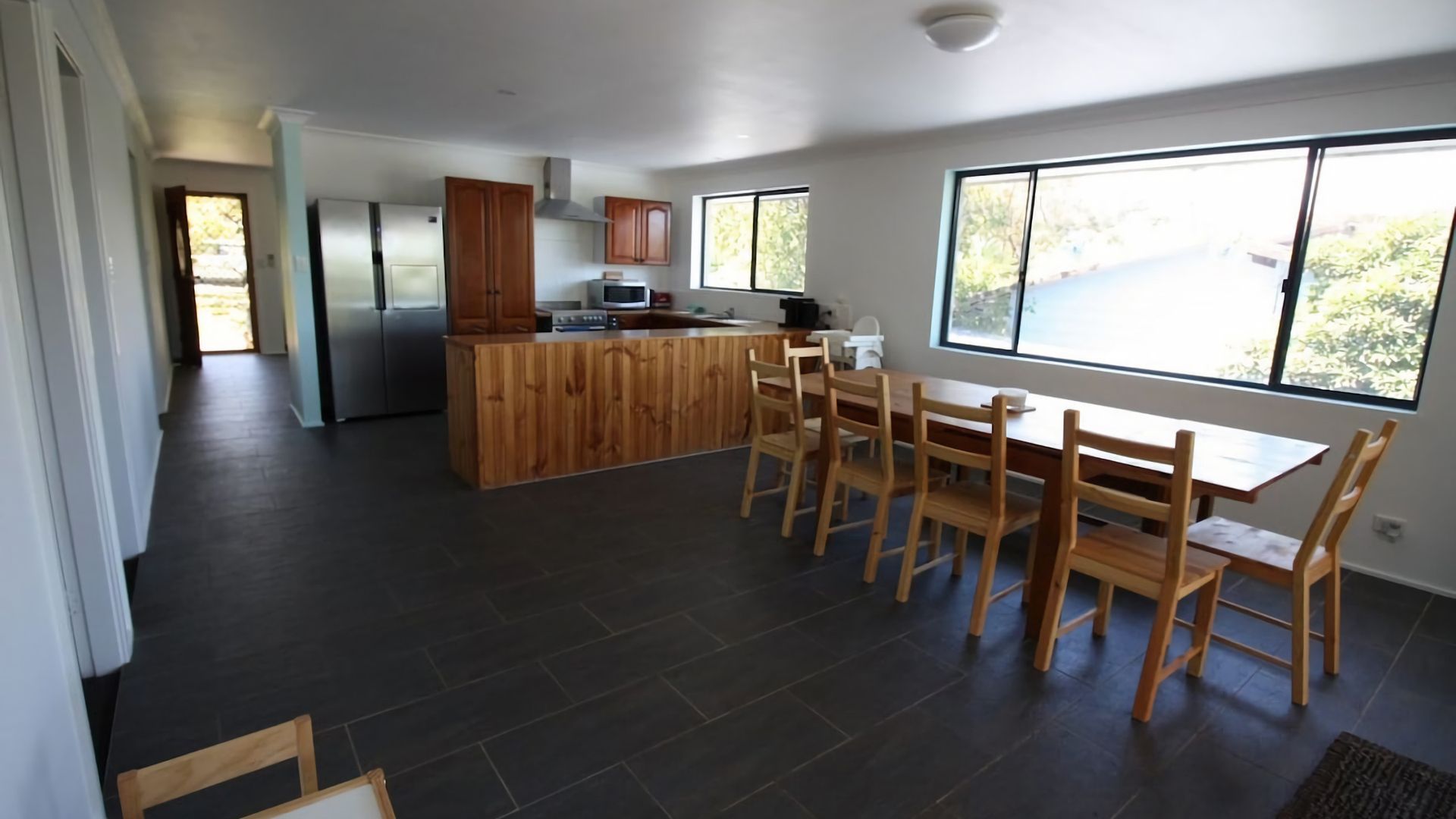 A modern kitchen with dark tiles, wooden cabinetry, a central island, and a dining area with chairs.