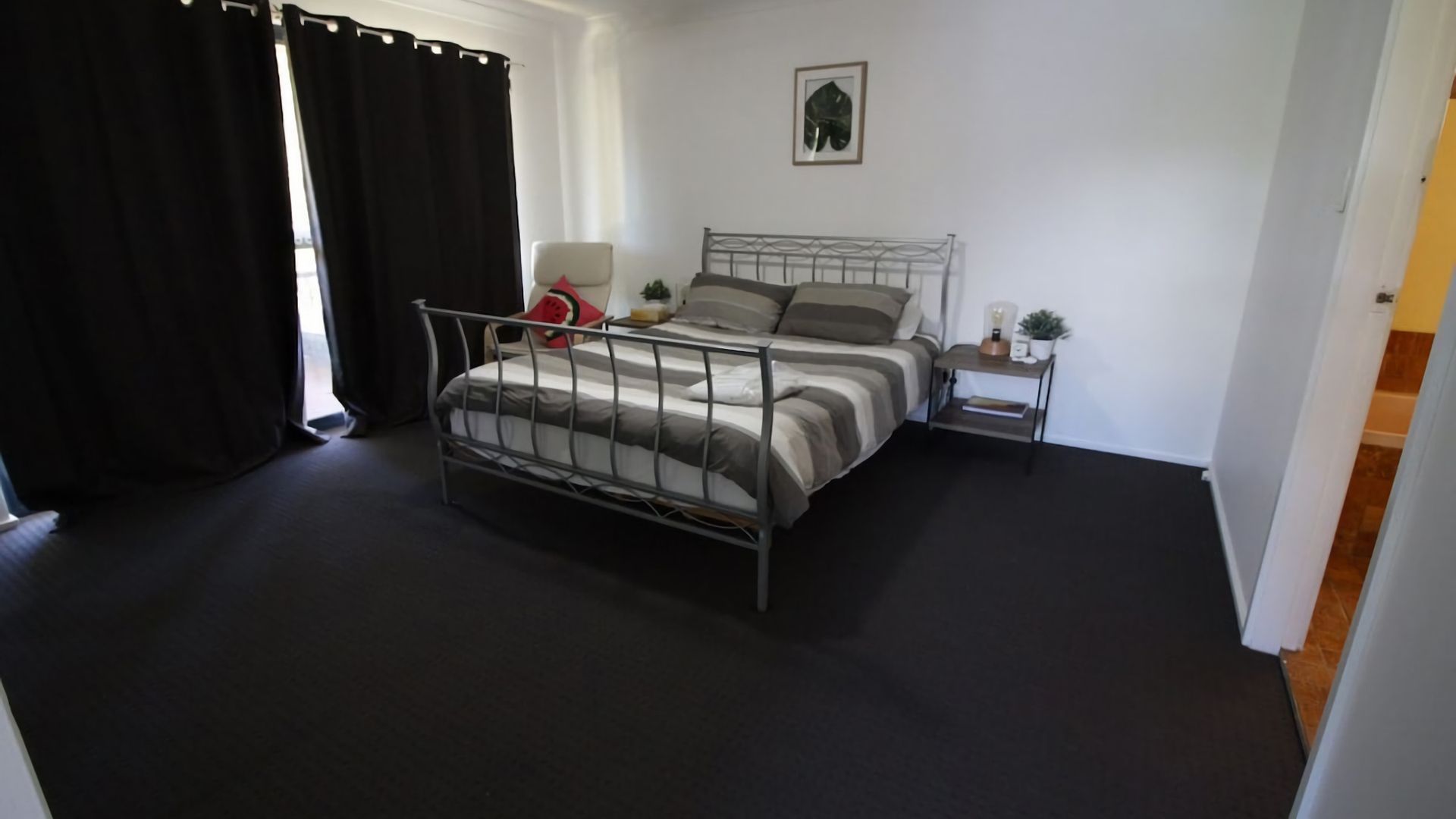 A bedroom with a metal bed frame, a bedside table with a lamp, and a small plant.