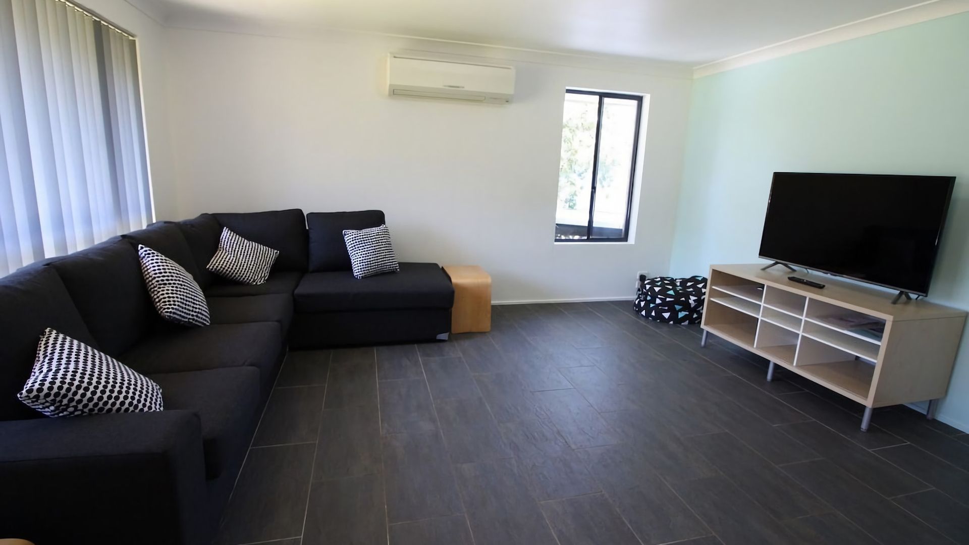 A modern living room with a sectional sofa, a flat-screen TV, and a wooden entertainment unit.