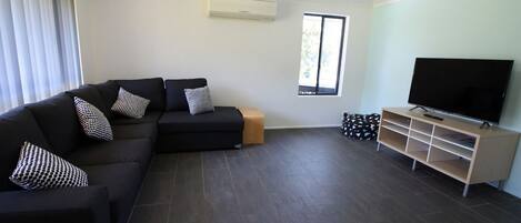Una sala moderna con un sofá modular, un televisor de pantalla plana y un mueble de entretenimiento de madera.