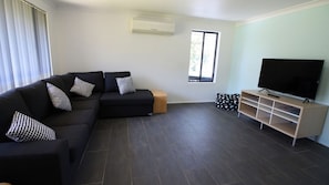 A modern living room with a sectional sofa, a flat-screen TV, and a wooden entertainment unit. - Holiday Haven is a spacious home (Manyana)