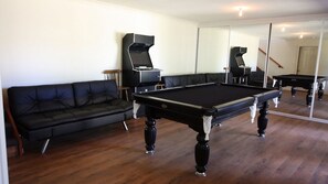 A room with a pool table, a black leather sofa, and a large mirror reflecting the room. - Holiday Haven is a spacious home (Manyana)