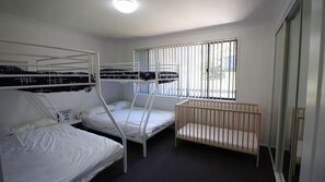 A room with bunk beds, a crib, and a window with blinds. - Holiday Haven is a spacious home (Manyana)