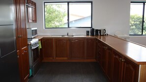 A kitchen with wooden cabinets, a stainless steel refrigerator, a microwave, a stove, and a window providing a view of greenery outside. - Holiday Haven is a spacious home (Manyana)