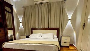 Una cama bien hecha con estructura de madera, una mesita de noche con lámpara y un aire acondicionado fijado a la pared.