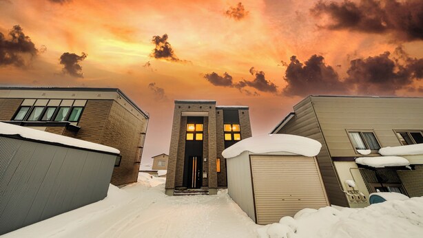 A building with a brick facade and a large entrance door, surrounded by snow. - ASTAGE VILLA KAMIFURANO (Kamifurano)