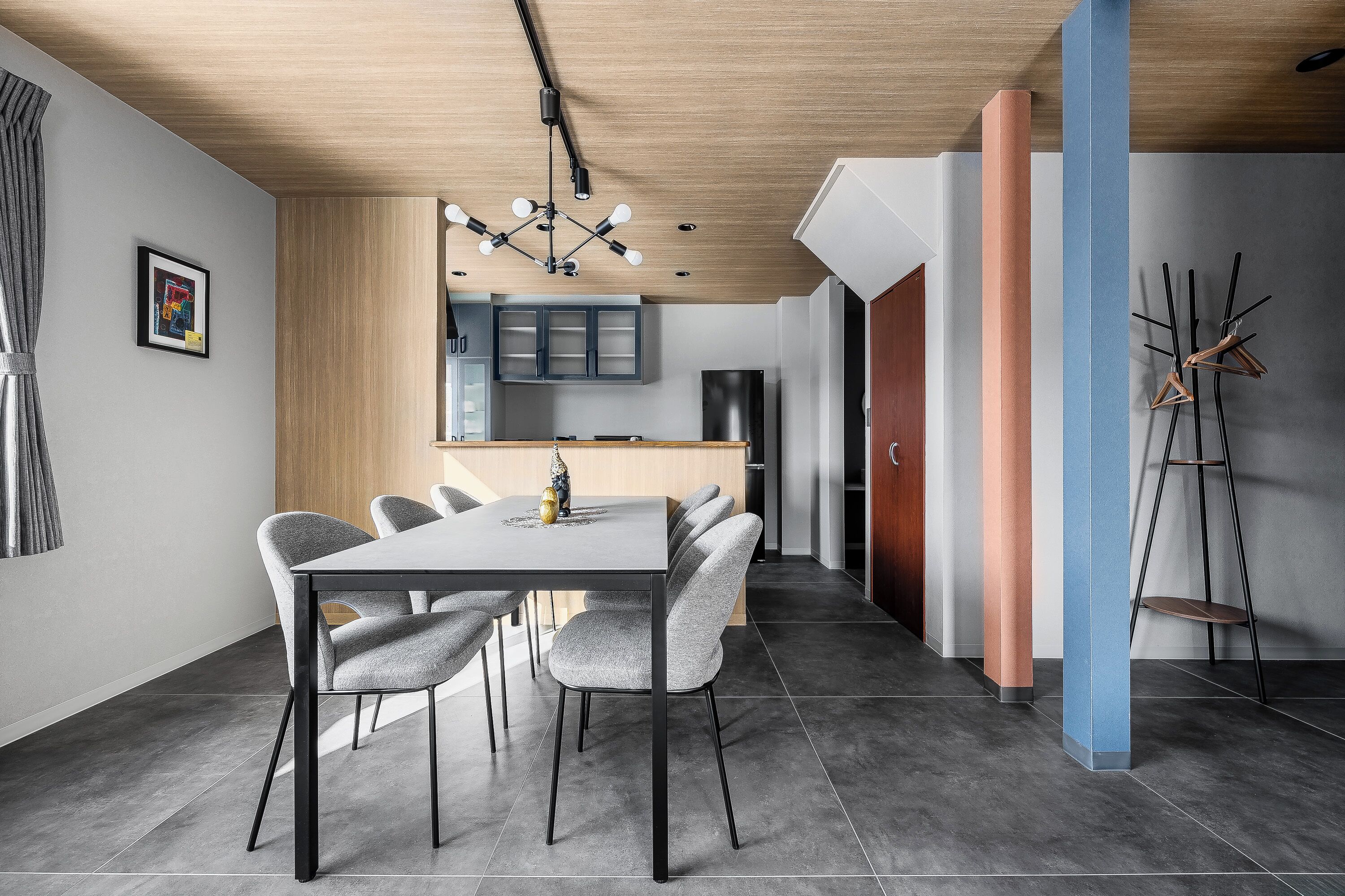 A modern dining area with a rectangular table, grey upholstered chairs, and a wooden ceiling.