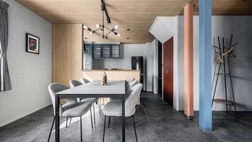 A modern dining area with a rectangular table, grey upholstered chairs, and a wooden ceiling.