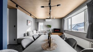 A modern living room with a long dining table, grey sofas, a TV, and a large window with curtains. - ASTAGE VILLA KAMIFURANO (Kamifurano)