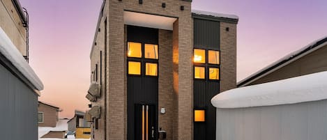 A modern building with a black door and windows, surrounded by snow.