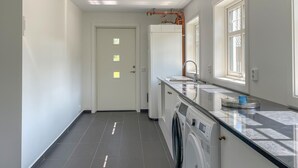 Een moderne keuken met een ingebouwde wasmachine en droger, een groot raam en een deur met kleine ruitjes.