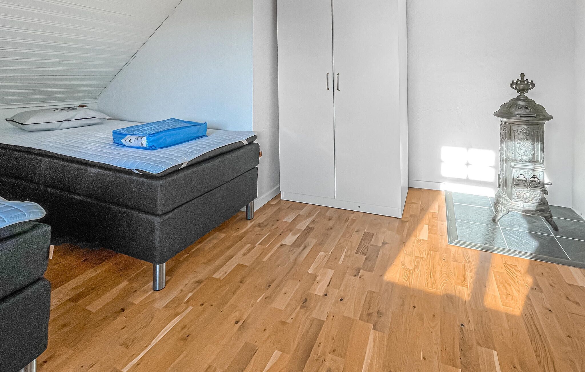 A bedroom with a bed, a wardrobe, a glass table with a decorative item, and a wooden floor.
