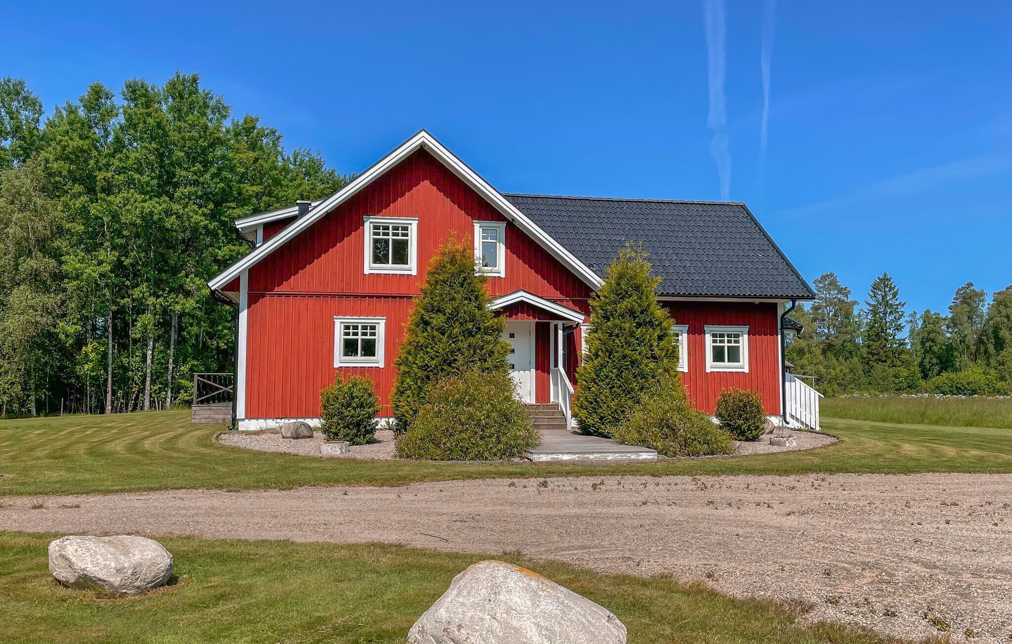 Une maison rouge à deux étages, avec un toit sombre, entourée d’une pelouse bien entretenue et d’arbres.
