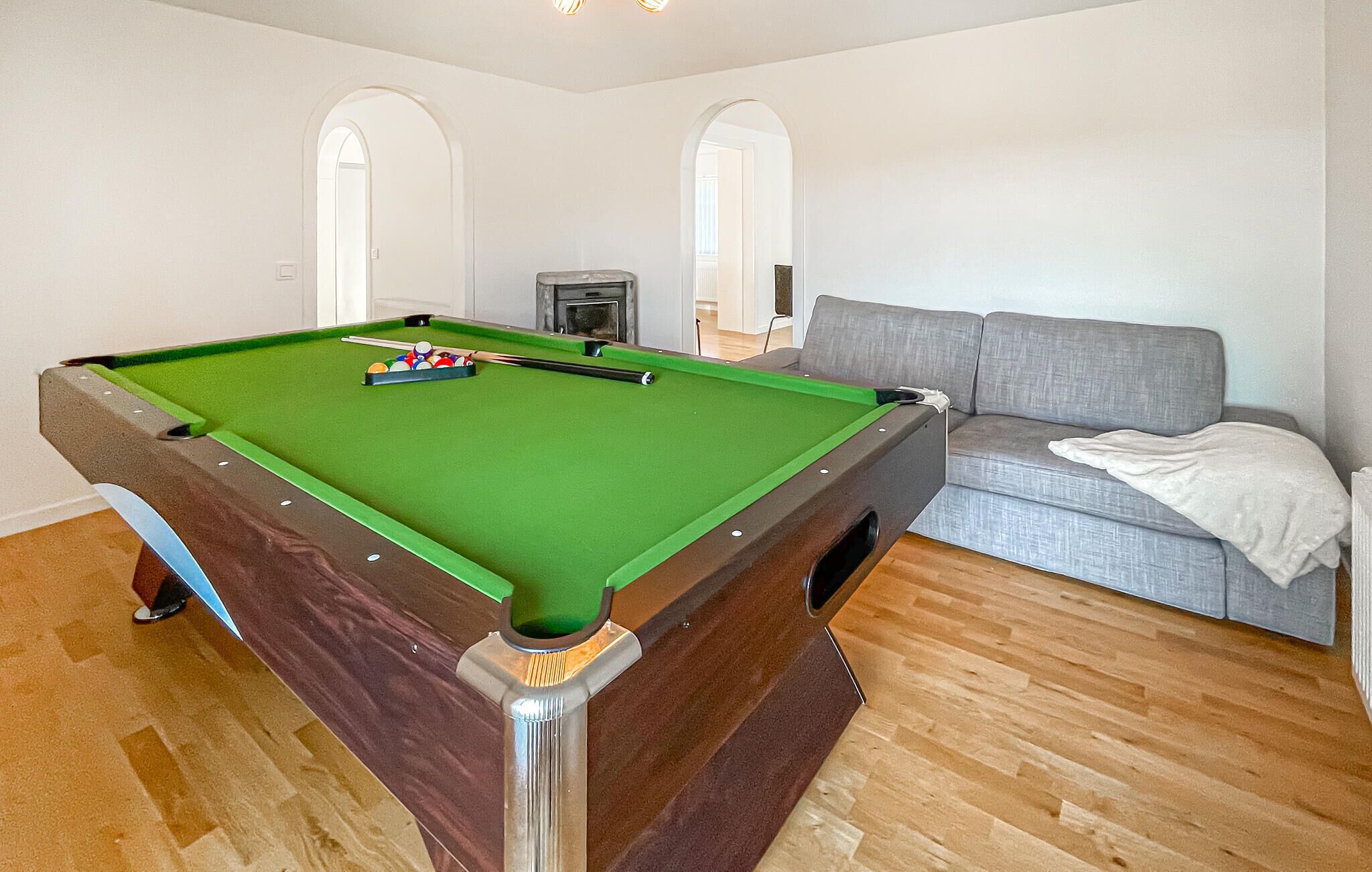 Une table de billard dans une pièce avec un canapé gris et un plancher en bois.