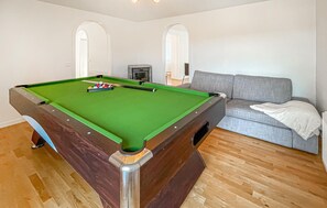 Une table de billard dans une pièce avec un canapé gris et un plancher en bois.