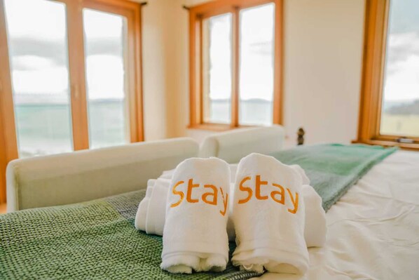 Een hotelkamer met een bed, een groene handdoek en twee handdoeken met de tekst 'stay' erin geborduurd.