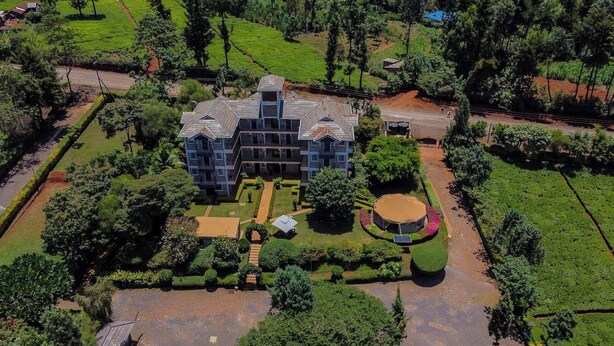 A large, multi-story building with a symmetrical facade, surrounded by well-maintained gardens and a circular water feature. - Goshen Farm Hotel (Kiriaini)