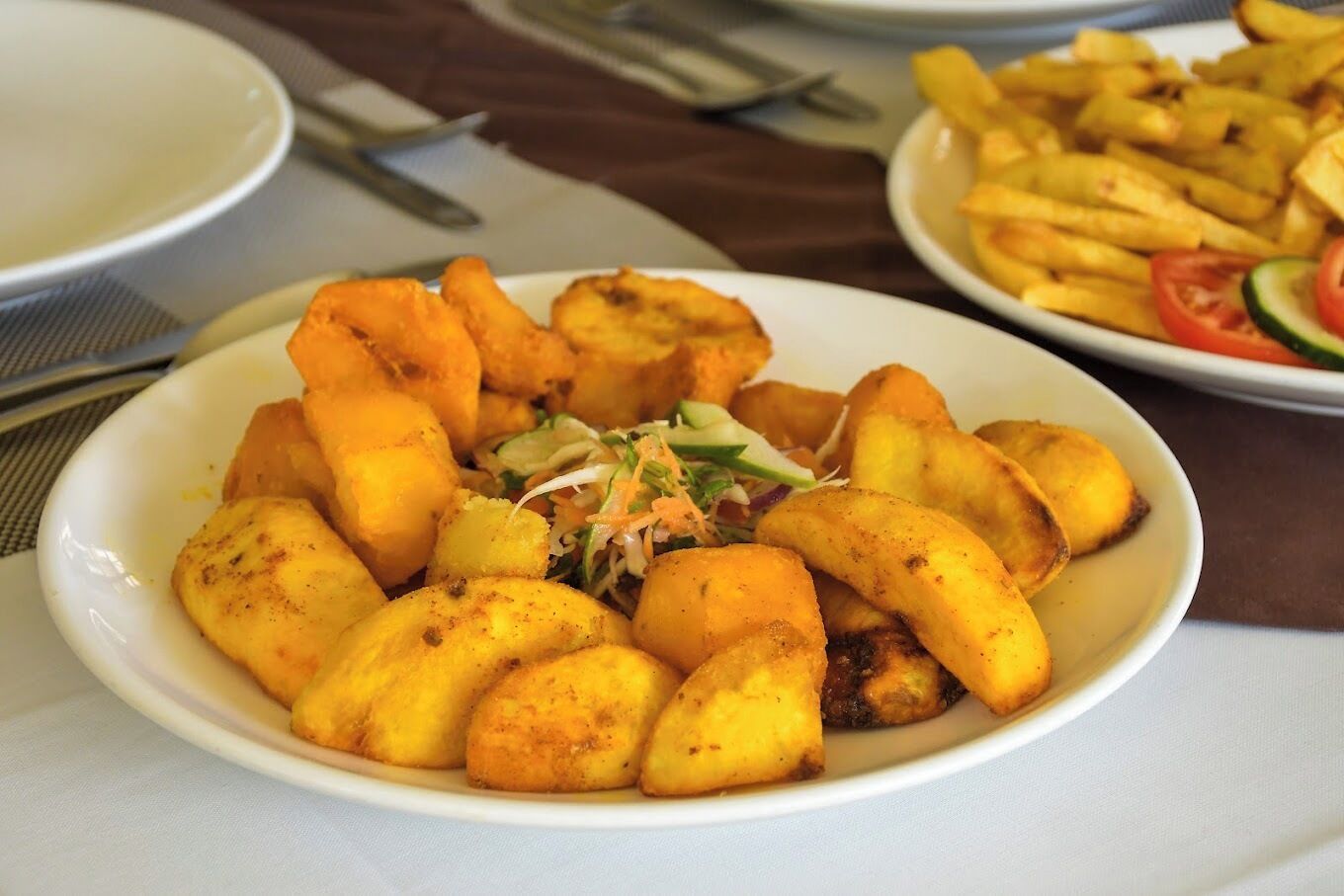 Ein Teller gebratene Kochbananen, dazu ein Salat und ein Teller Pommes.
