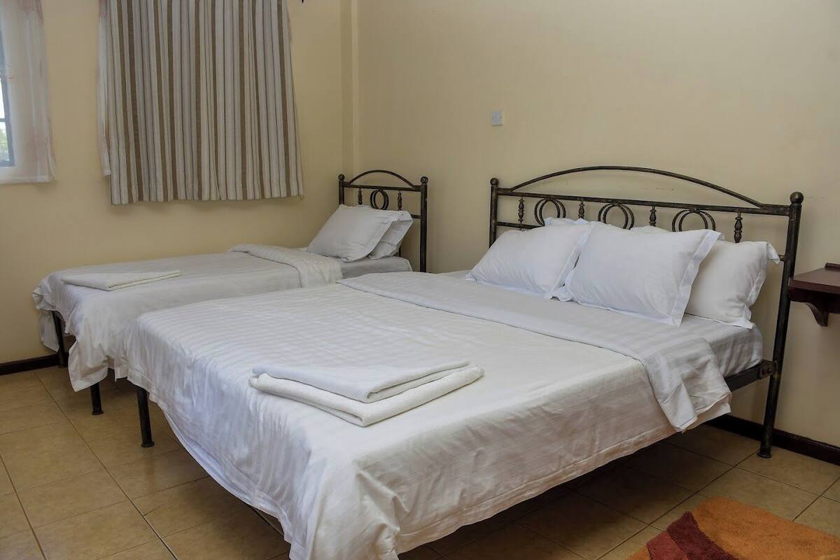 A room with two beds, each with white bedding and pillows, a metal headboard, and a small bedside table.