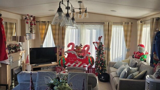 Un salon avec un téléviseur, un canapé, une table à manger avec des chaises et un sapin de Noël.