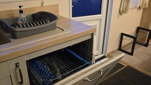 Une cuisine équipée d’un lave-vaisselle encastré, d’un égouttoir et d’une fenêtre donnant sur l’extérieur.