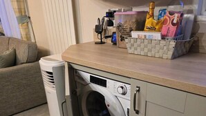 Une cuisine compacte équipée d’un lave-linge intégré, d’un petit réfrigérateur et d’un plan de travail sur lequel sont disposés divers objets.