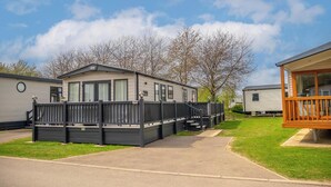 Une maison mobile avec une cour clôturée, une véranda et une maison voisine.
