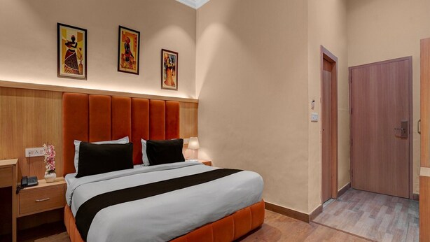 Une chambre d’hôtel avec un grand lit, une tête de lit en bois et une table de chevet avec une lampe. Trois œuvres d’art encadrées sont accrochées au mur au-dessus du lit.