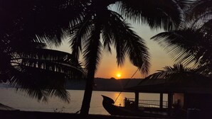 A sunset view with a boat docked near a building with a thatched roof. - Chaitanya Nyahari Niwas (Malvan)
