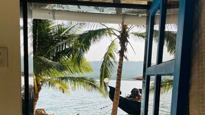 A view from a room with a blue door leading to a balcony overlooking a pool and a beach with palm trees. - Chaitanya Nyahari Niwas (Malvan)