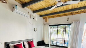 A spacious bedroom with a large bed, a ceiling fan, and a view of the outdoors through a sliding glass door. - Chaitanya Nyahari Niwas (Malvan)